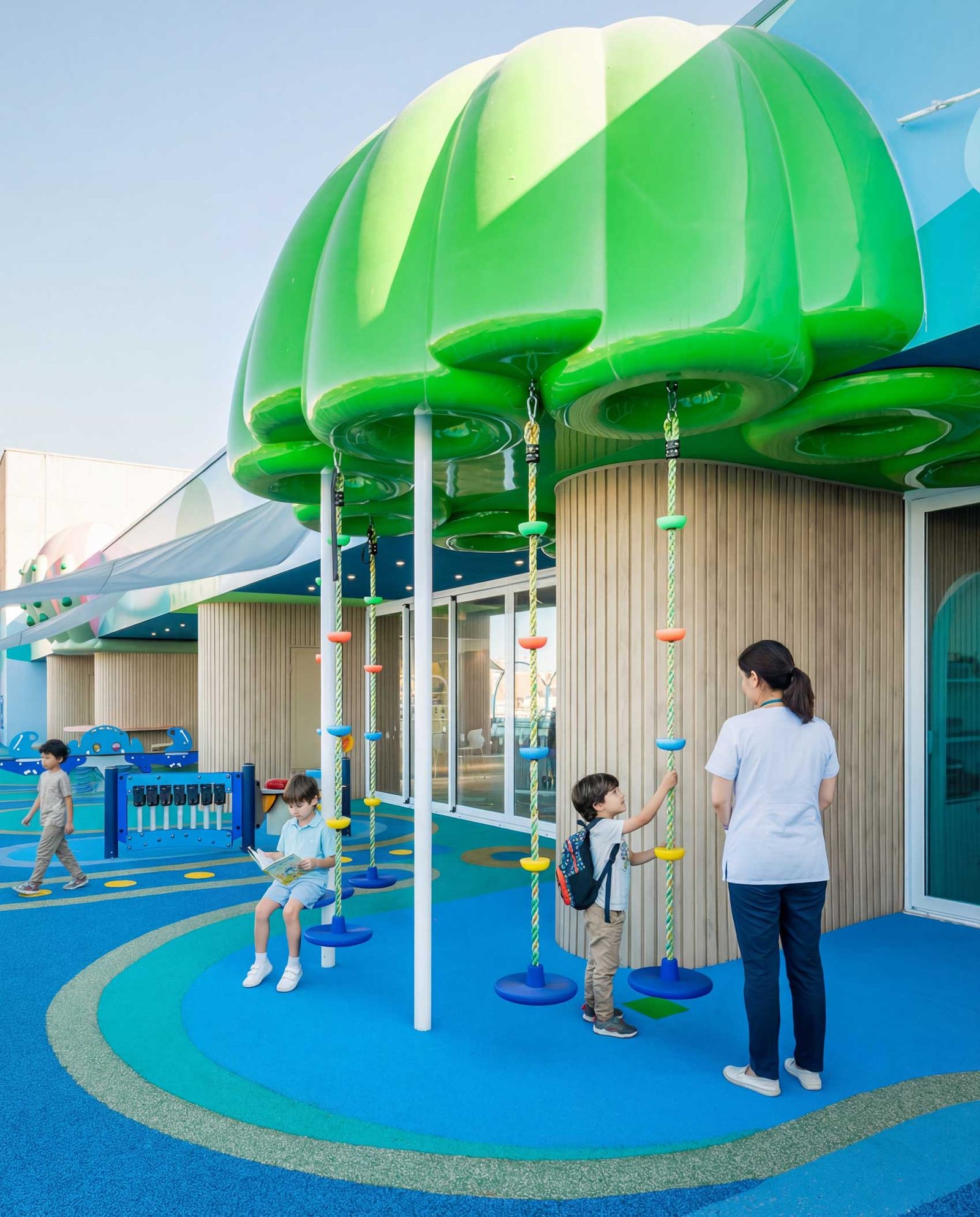 The rounded green canopy structure above the blue play floor, with a child and a member of staff below.