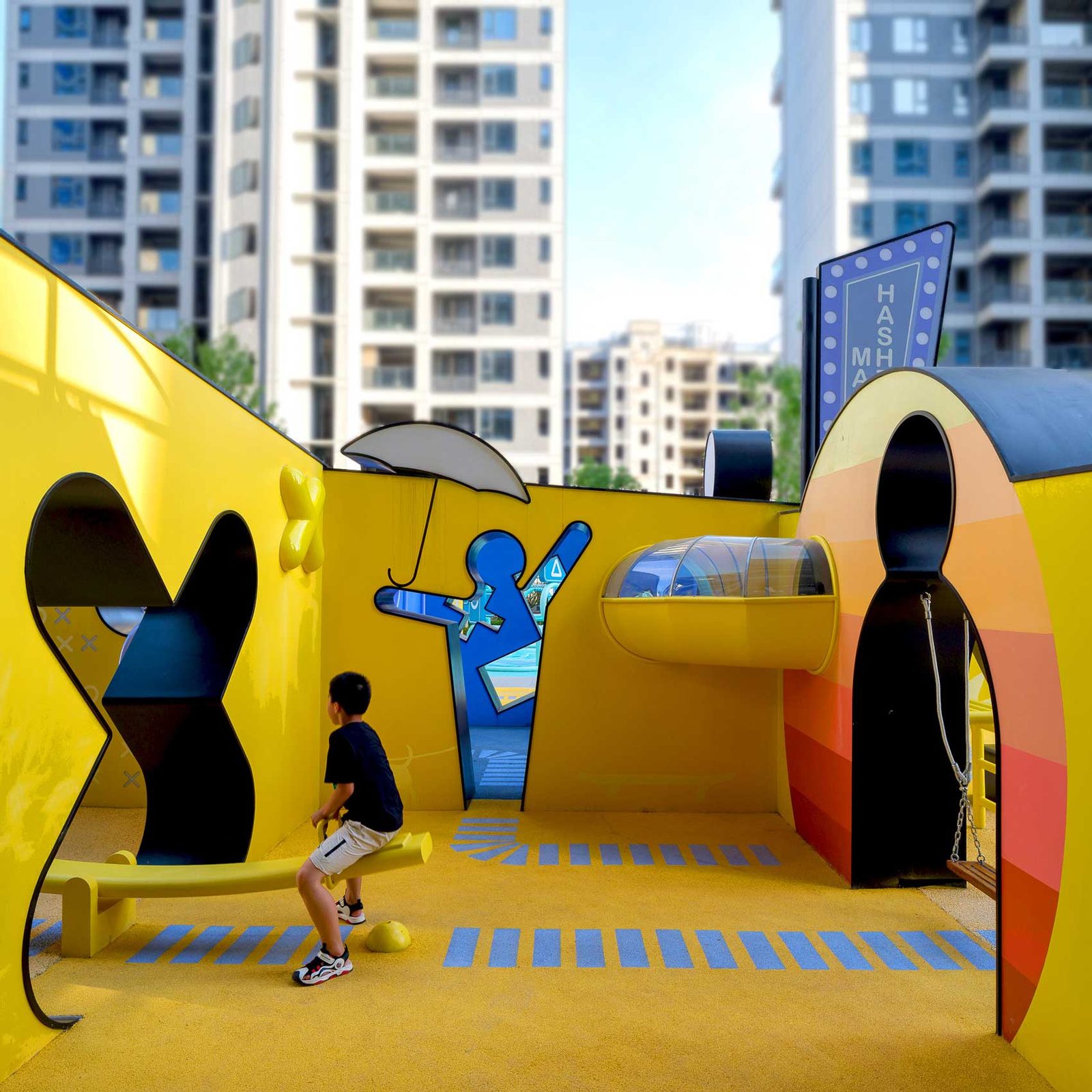 A child playing inside a yellow volume with arched openings and graphic wall figures.