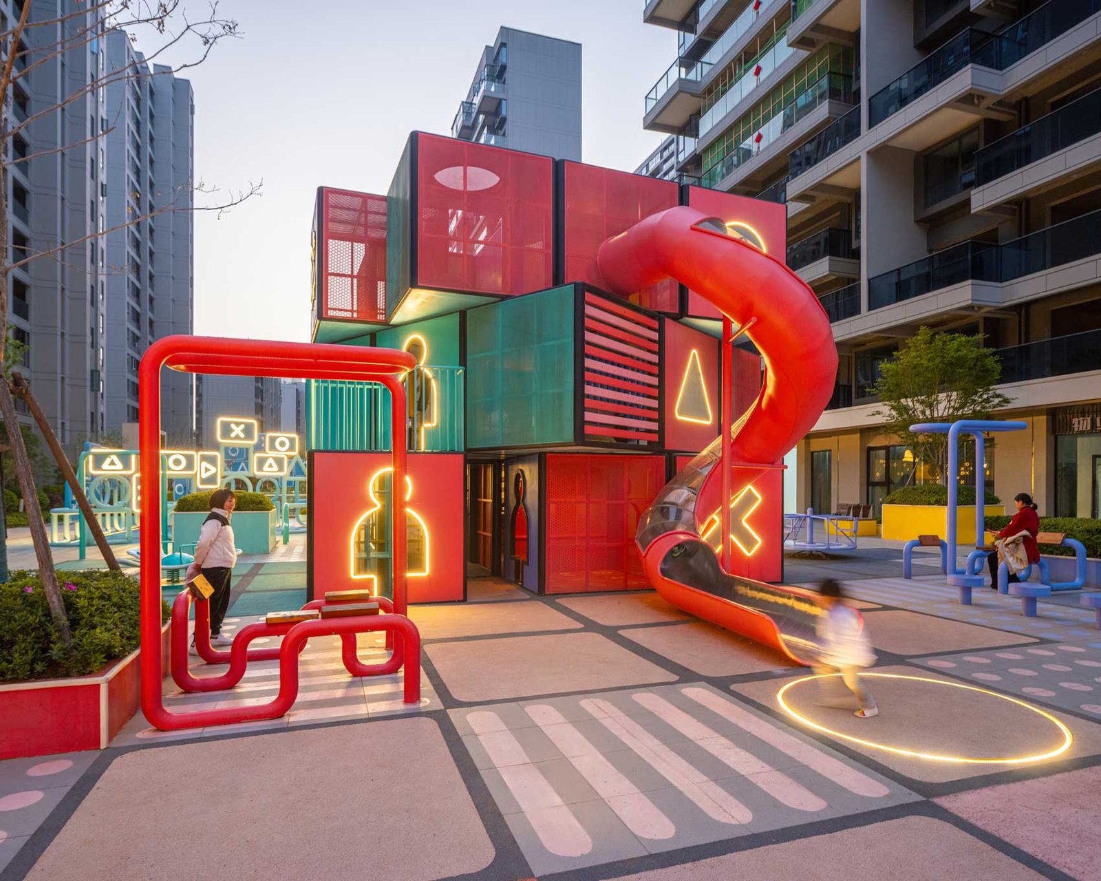 A red steel play structure with a spiral slide, set against the neighbouring apartment blocks.