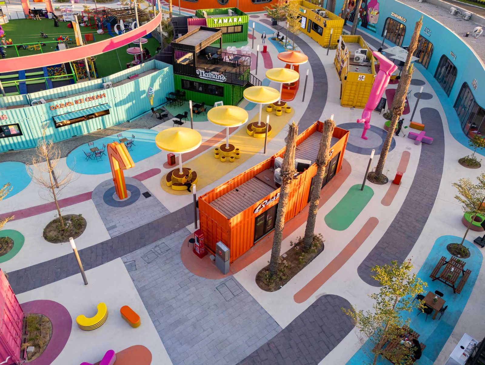 A plaza of container units, yellow parasols and planting on the coloured pavement.